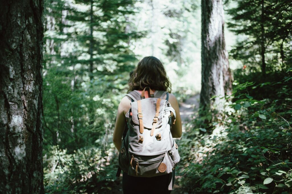 A woman carrying a backpack walks along a forest path, enveloped by vibrant greenery and the sounds of nature.