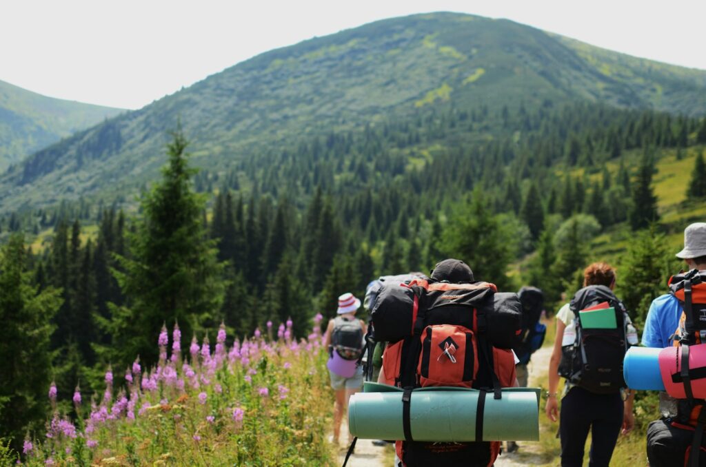 Group of people carrying hiking bags walking on hilltop during daytime