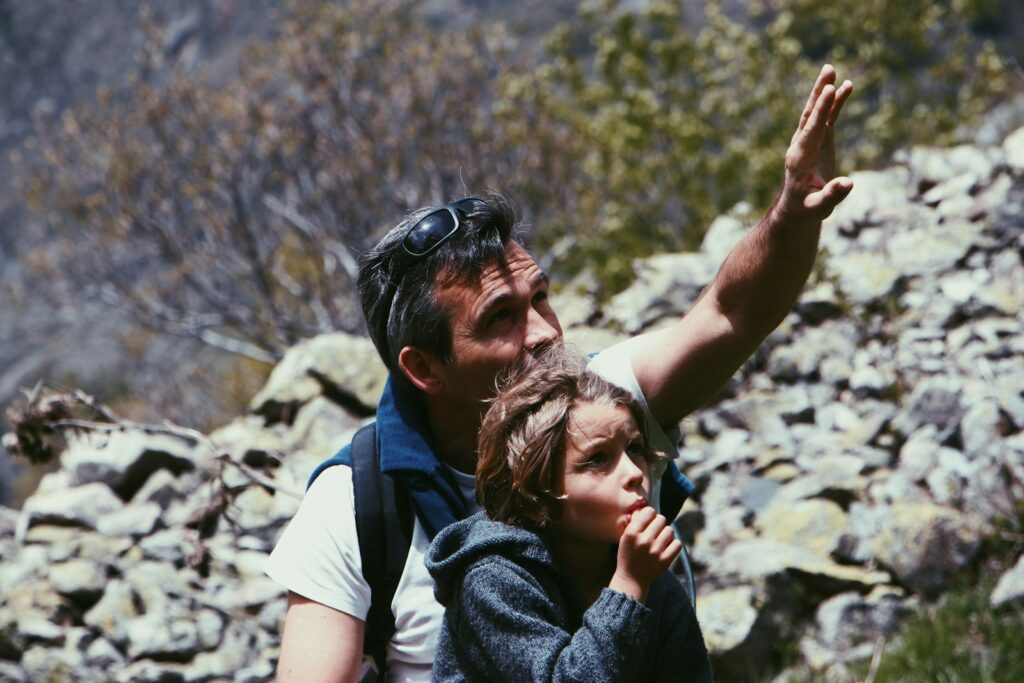 Boy standing in front of man near rocky terrain during daytime.