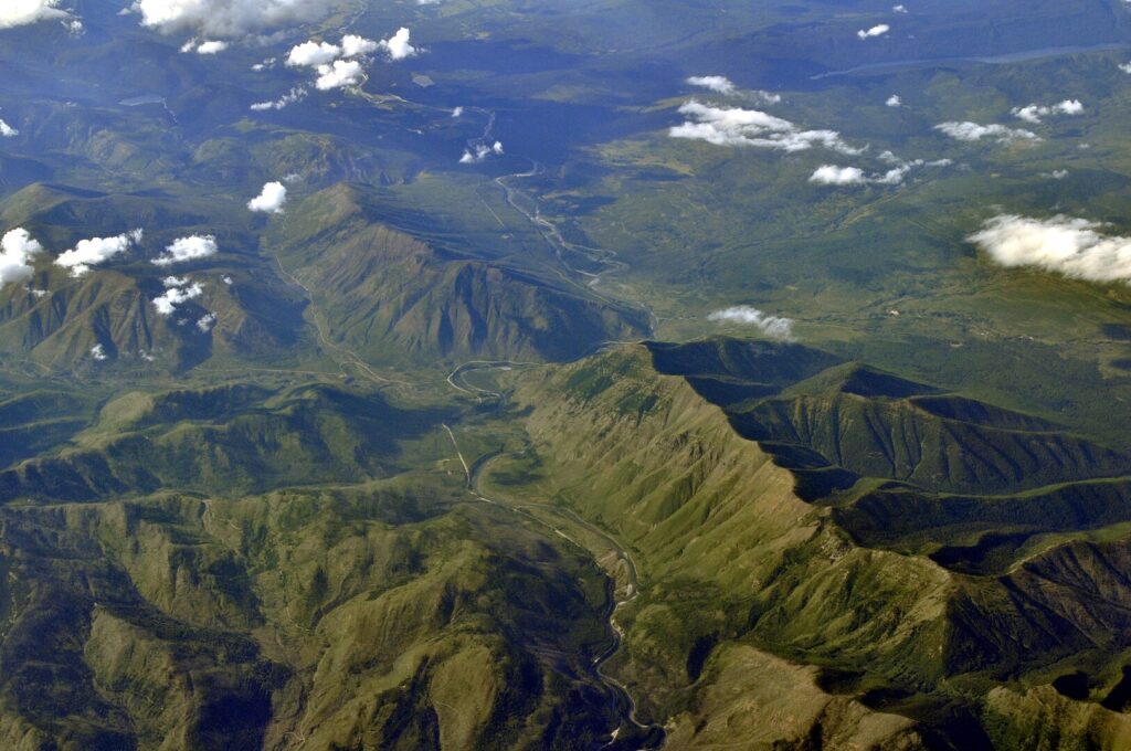 Scenic mountain landscape seen from an airplane, featuring towering peaks and expansive valleys against a bright sky.