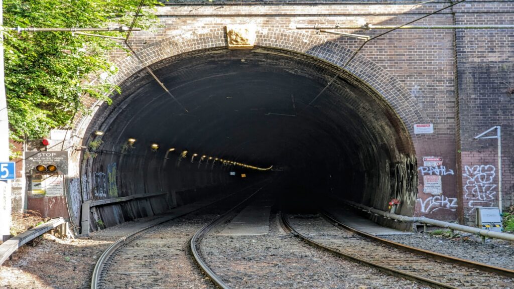 A train enters a dark tunnel, displaying a sign on its side, emphasizing its journey through the underground passage.