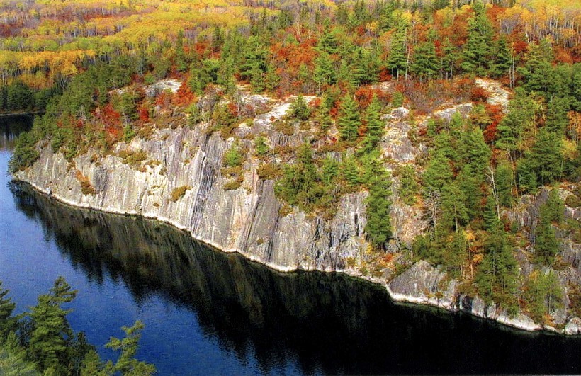 A serene lake framed by vibrant fall foliage and rugged rocks, reflecting the warm colors of autumn.