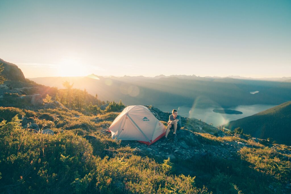 Man sitting on stone beside white camping tent.