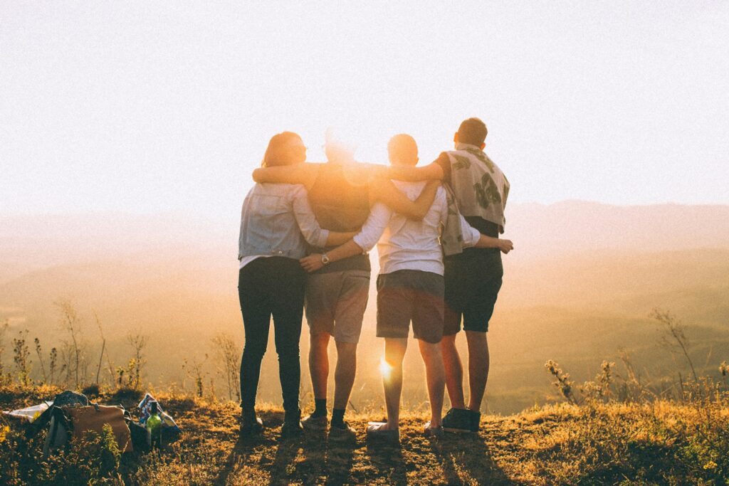 Four person hands wrap around shoulders while looking at sunset.