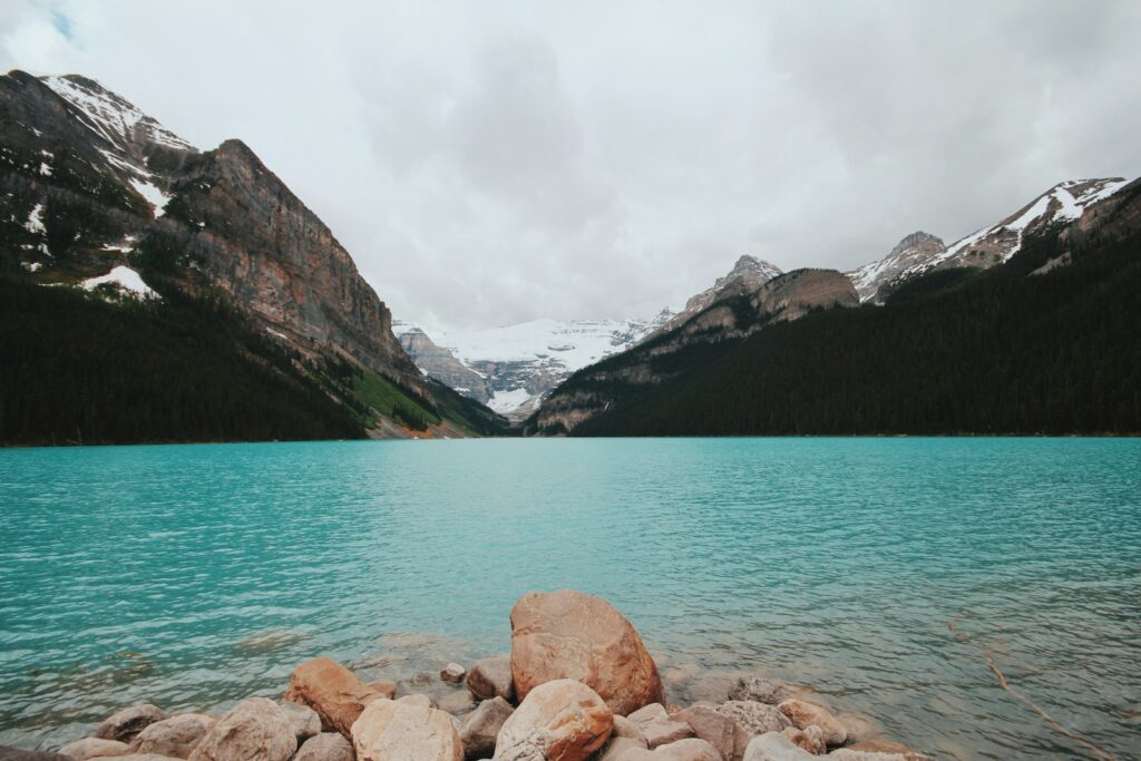 brown rocks beside blue lake near white snowy mountain at daytime
