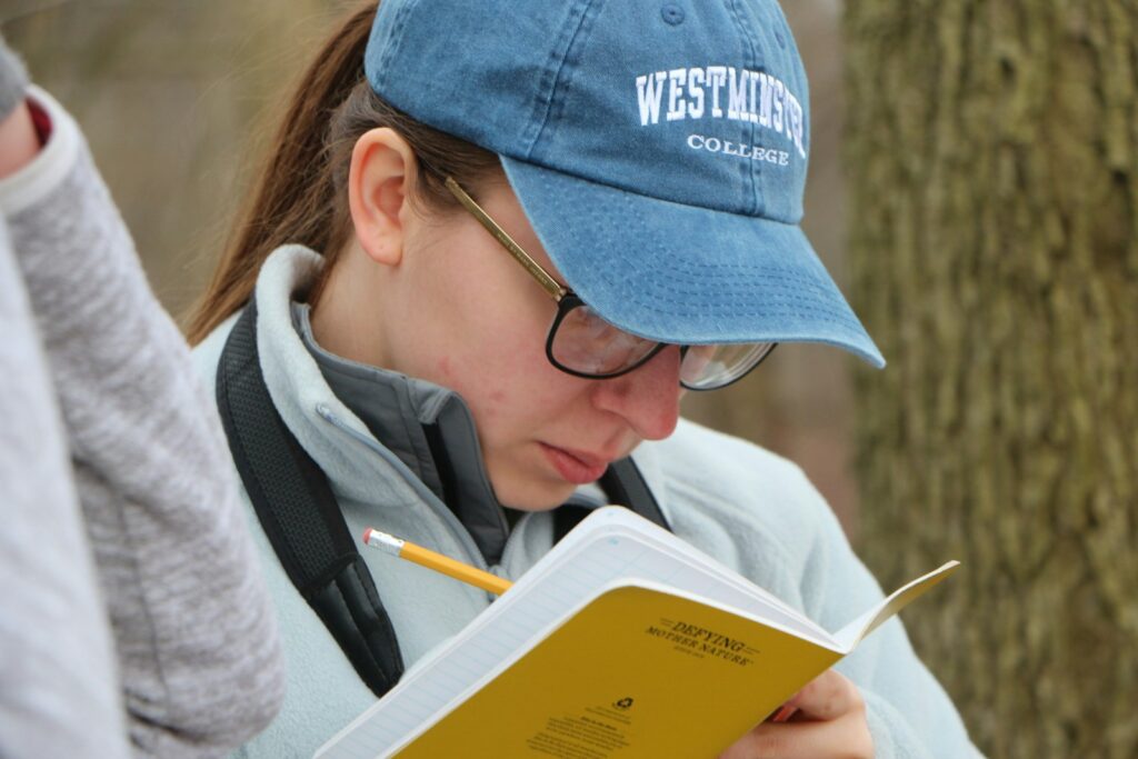 Woman in blue knit cap and blue framed eyeglasses reading book.
