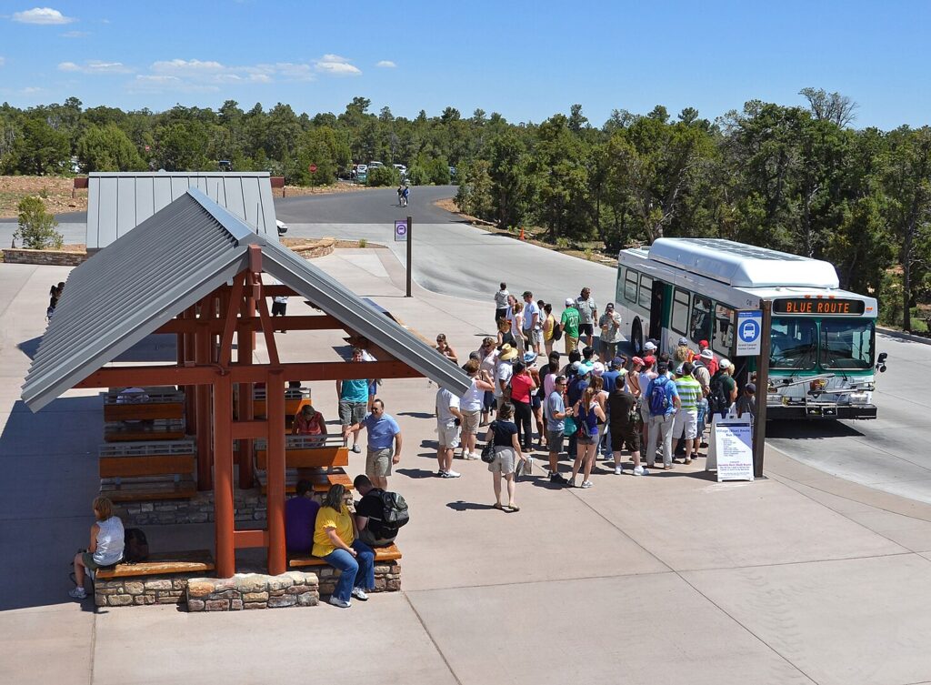 A diverse group of people waiting at a bus stop, engaged in conversation and checking their phones.