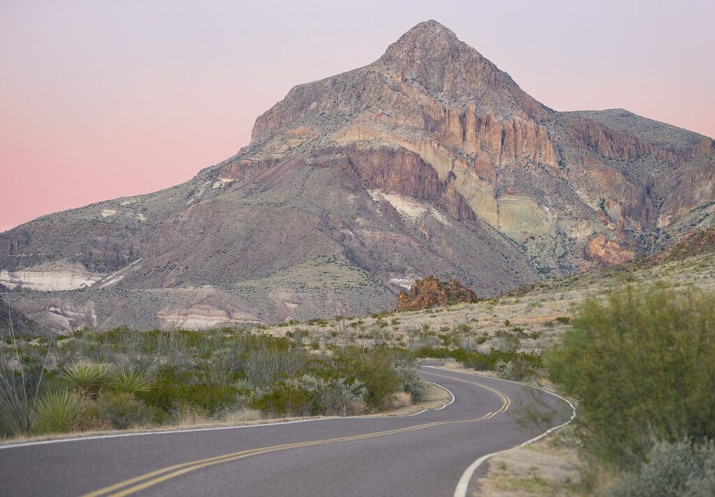 A scenic view of a mountain with a winding road cutting through it, captured during sunset at Big Bend National Park.