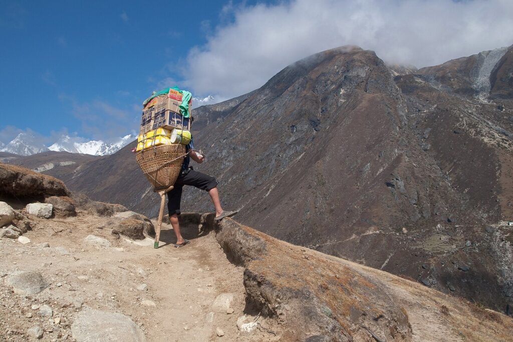 A man climbs a steep mountain path, shouldering a large backpack, showcasing resilience and determination in nature.
