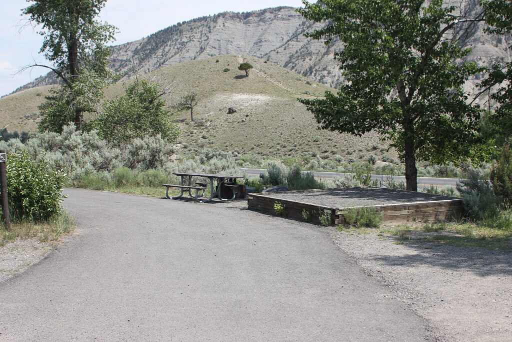A scenic view of a road in Mammoth Hot Springs Campground featuring a picnic table and a bench for relaxation.