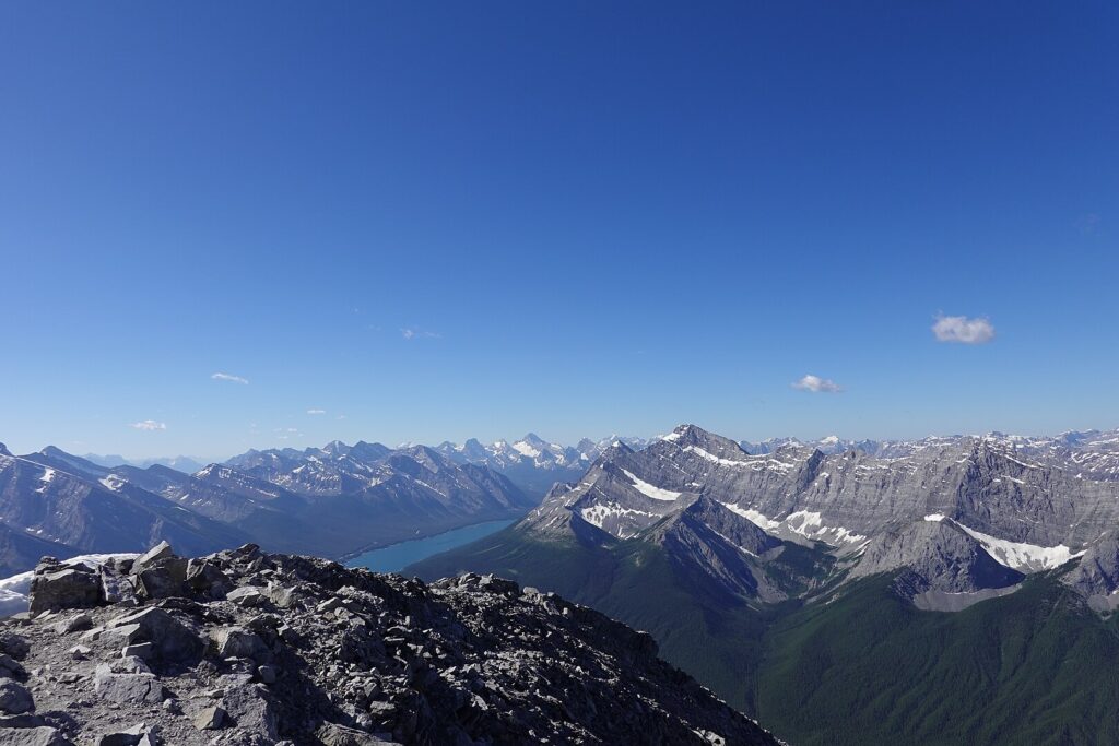 Panoramic vista of the Rocky Mountains and a sparkling lake, captured from the mountain peak, highlighting breathtaking beauty.