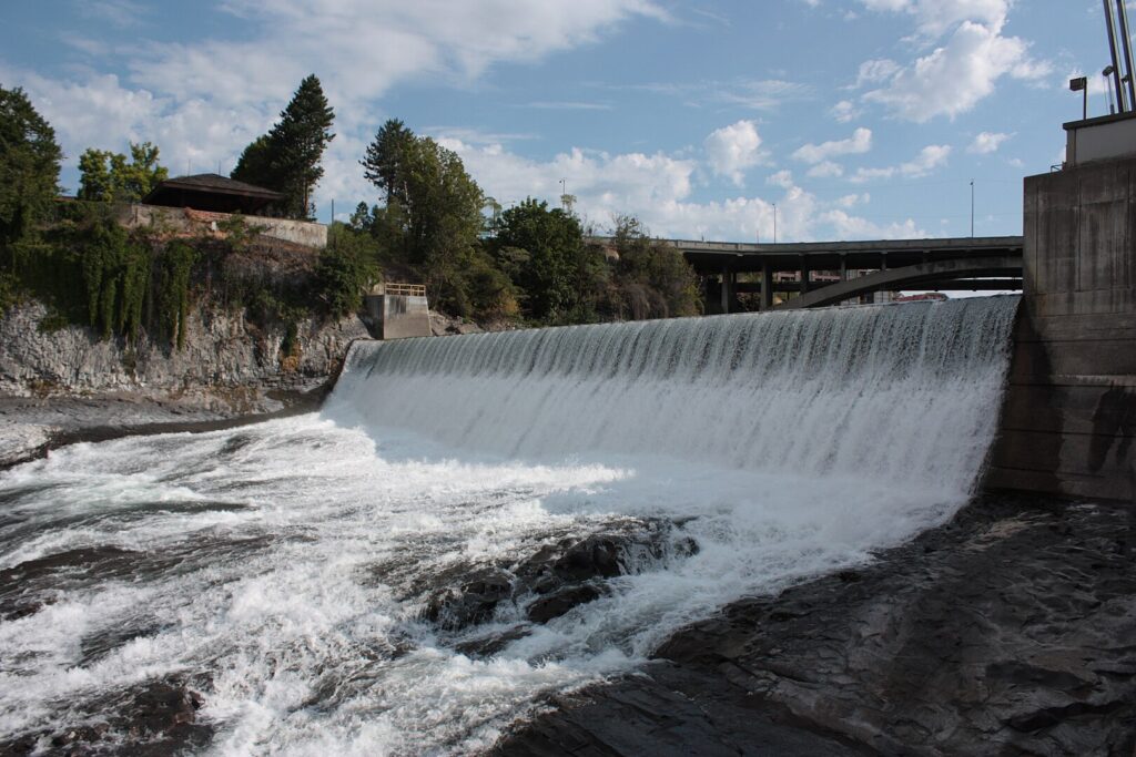 A majestic waterfall cascades down rocks, with a scenic bridge arching gracefully in the background.
